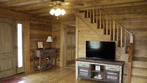 A wooden interior with a staircase, a television on a wooden cabinet, and a lamp on a side table. - Charming Country Cabin in Quaint Texas Town (Fayetteville)