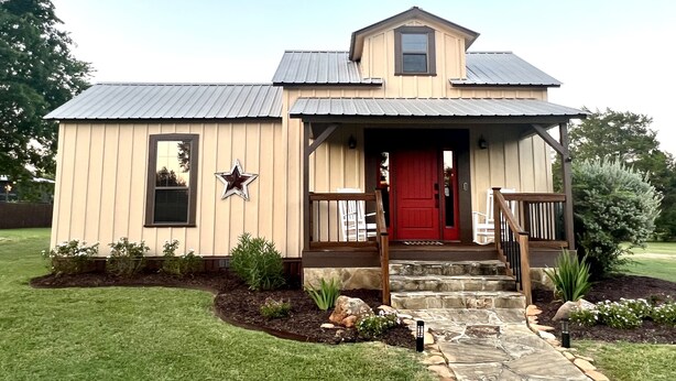 A single-story house with a red door, a star decoration, and a stone pathway leading to the entrance. - Charming Country Cabin in Quaint Texas Town (Fayetteville)