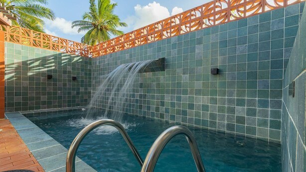 Une piscine agrémentée d’une cascade, entourée d’un mur carrelé et d’une clôture décorative.