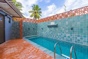 Ein Schwimmbecken mit einer gefliesten Wand, einer Holzterrasse und einer Metallleiter.