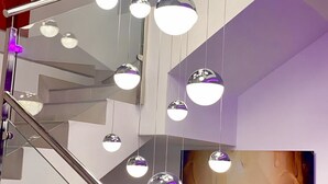 Un interno moderno con una scala, diverse lampade sferiche sospese e un'ampia opera d'arte incorniciata a parete.
