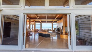 A spacious interior with a large seating area, a fireplace, and a view of the ocean. - Oceanside Escape • An Oceanfront Gathering Place (Arch Cape)