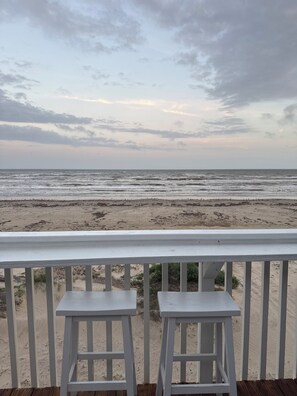 Blick auf einen Strand von einem Balkon mit zwei weißen Hockern.