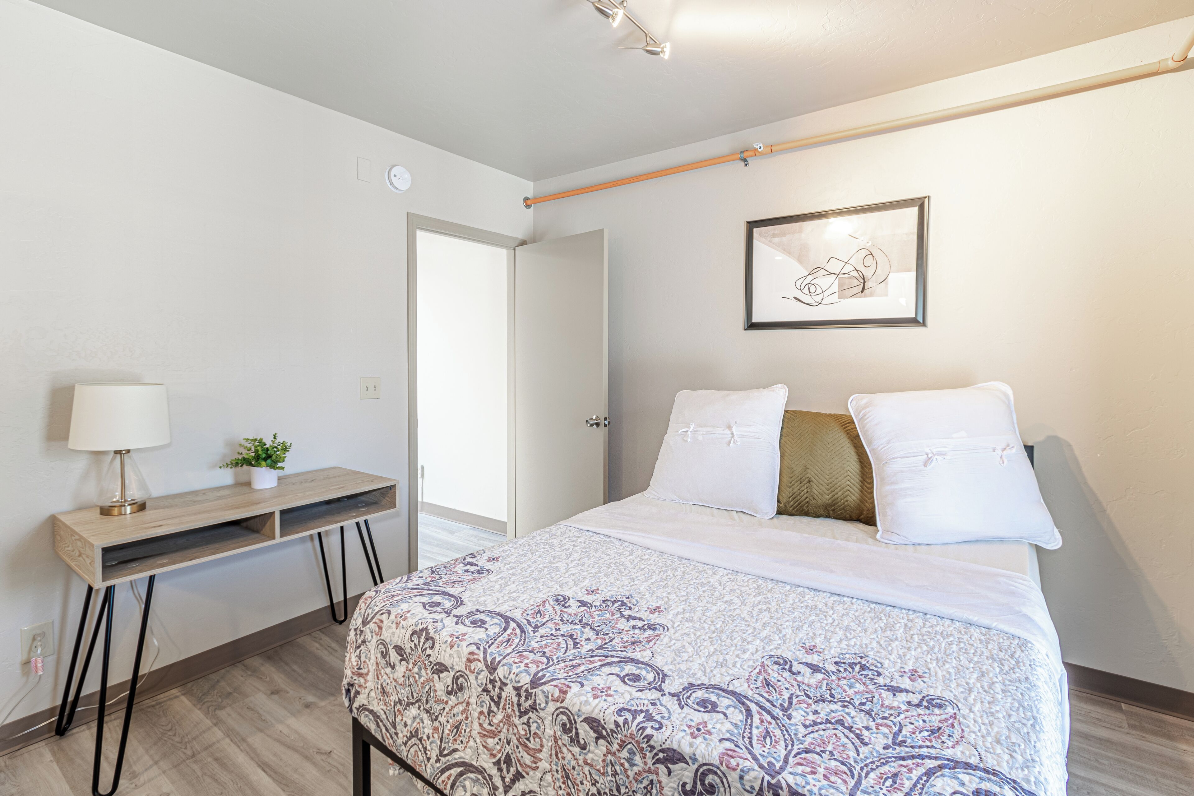 A bedroom with a bed, bedside table, lamp, and a framed picture on the wall.