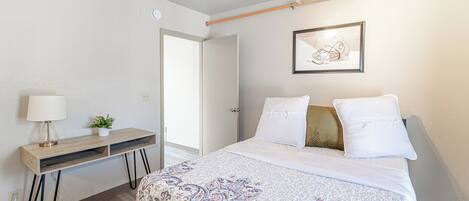 A bedroom with a bed, bedside table, lamp, and a framed picture on the wall.
