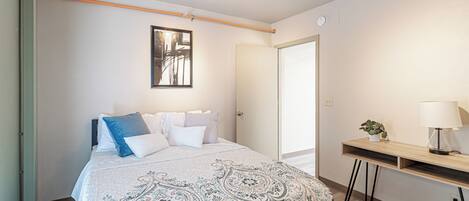 A bedroom with a bed, bedside table, lamp, and a door.