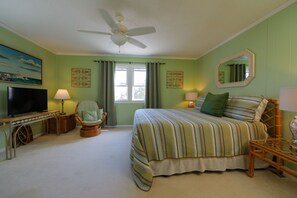 A bedroom with a bed, a chair, a TV, and a ceiling fan. - Family beach cottage poised between the ocean, hiking, biking, eateries & shops (Emerald Isle)