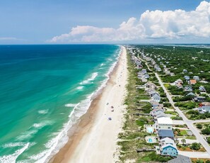 An aerial view of a coastal residential area with houses along the beach, clear skies, and a calm sea. - Family beach cottage poised between the ocean, hiking, biking, eateries & shops (Emerald Isle)