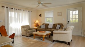 Ein Wohnzimmer mit Deckenventilator, einer Sofagarnitur, einem Couchtisch und einem Essbereich mit Stuhl und Tisch.