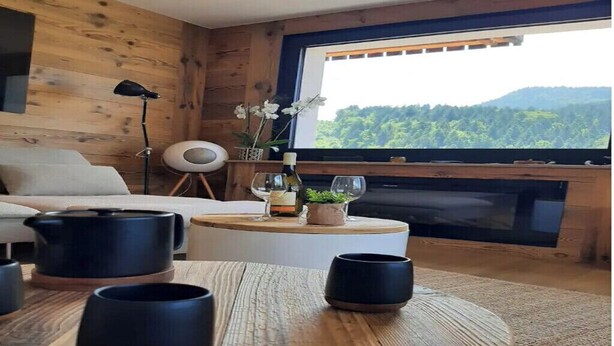Une pièce chaleureuse au décor intérieur en bois, avec une table ronde en bois, des tasses noires, une bouteille de vin et un verre posés sur la table.