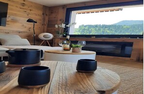 A cozy room with a wooden interior, a round wooden table with black cups, a bottle of wine, and a glass on the table.
