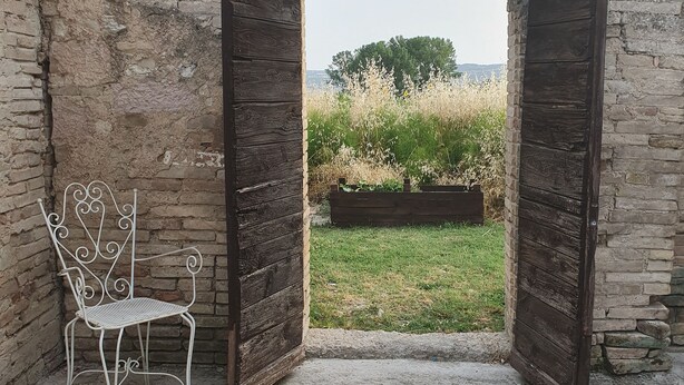 An open doorway leading to a grassy area with a bench and a wooden structure. - The pigsty in the valley of Assisi (Assisi)