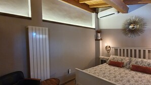A bedroom with a wooden ceiling, a bed with floral bedding, a bedside table, and a wall-mounted light fixture. - The pigsty in the valley of Assisi (Assisi)