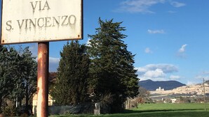 A sign reading "VIA S. VINCENZO" with a view of a town and mountains in the background. - The pigsty in the valley of Assisi (Assisi)