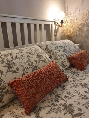 Un lit avec une literie à motifs floraux, une tête de lit blanche et deux coussins décoratifs.