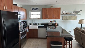 A modern kitchen with wooden cabinets, a black refrigerator, a sink, and a coffee maker. - Direct Oceanfront  South Cocoa Beach. Watch launches from Balcony. (Cocoa Beach)