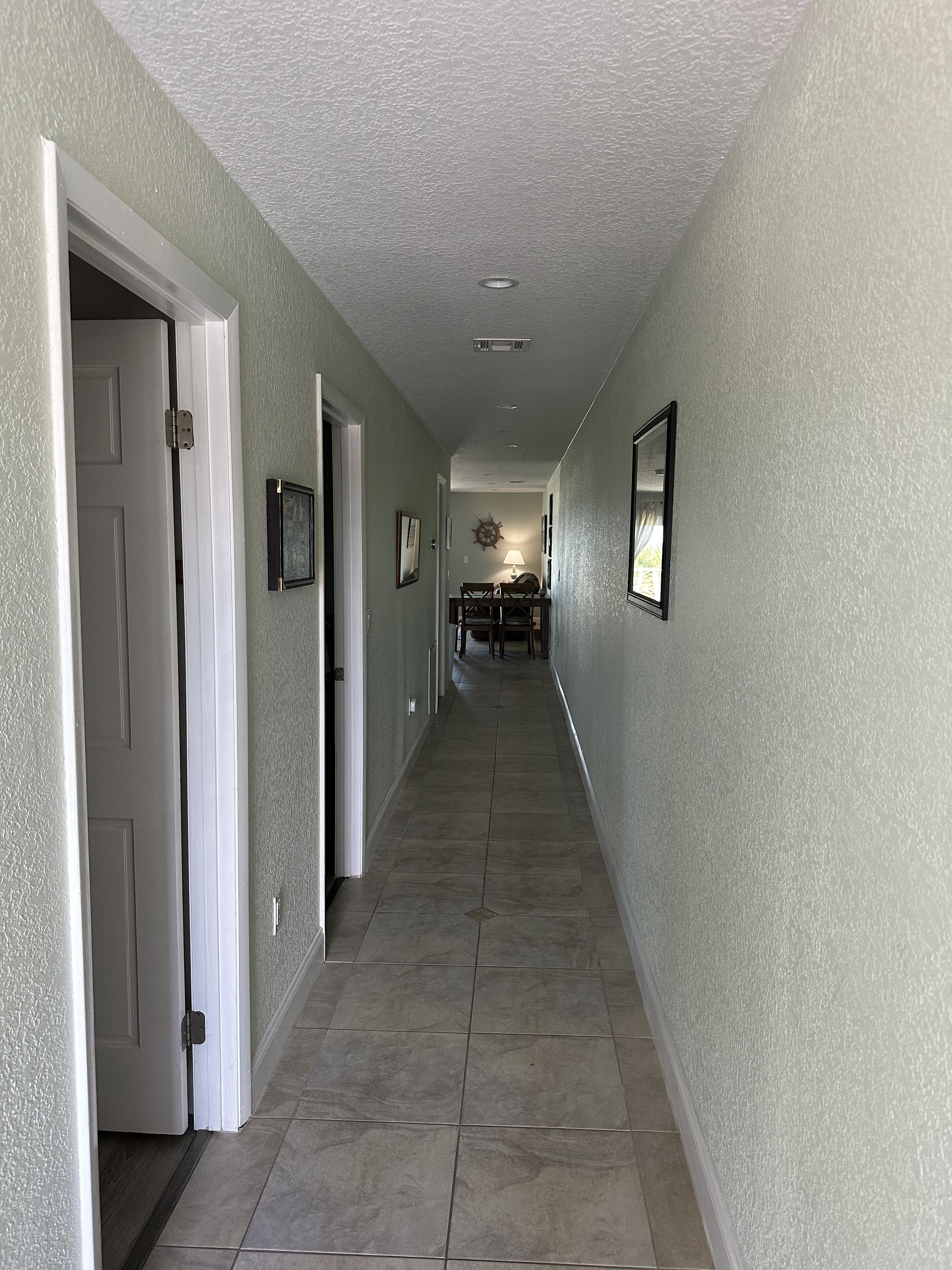 A hallway with a tiled floor, white walls, and a dining area in the distance.