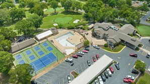 Vista aèria d'un camp de golf amb una pista de tennis, zona d'aparcament i edificis.
