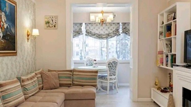 Een woonkamer met een hoekbank, een eettafel met stoelen, een kroonluchter en een open haard.