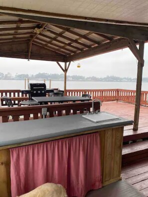 Une terrasse extérieure équipée d’un barbecue, de sièges et offrant une vue sur un plan d’eau.