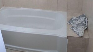 A bathroom with a bathtub, tiled walls, and a towel on a box. - The beach is our back yard Apt #4A (Bahamas)