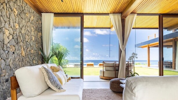 A modern living room with a stone wall, large windows, and a view of the ocean.