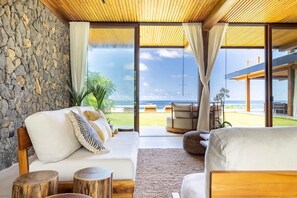 A modern living room with a stone wall, large windows, and a view of the ocean. - Luxury oceanfront villa, infinity pool + housekeeping & concierge included. (Los Pargos)