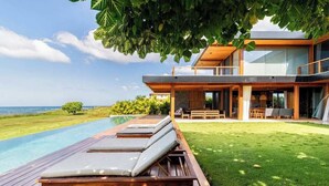 A modern house with a wooden deck, a swimming pool, and a view of the ocean.