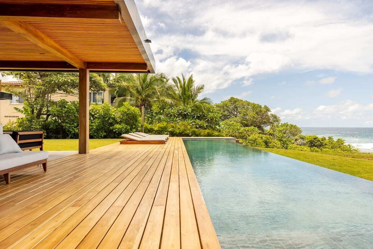 Eine Holzterrasse mit Liegestühlen und ein Pool, der bis zum Meer reicht.