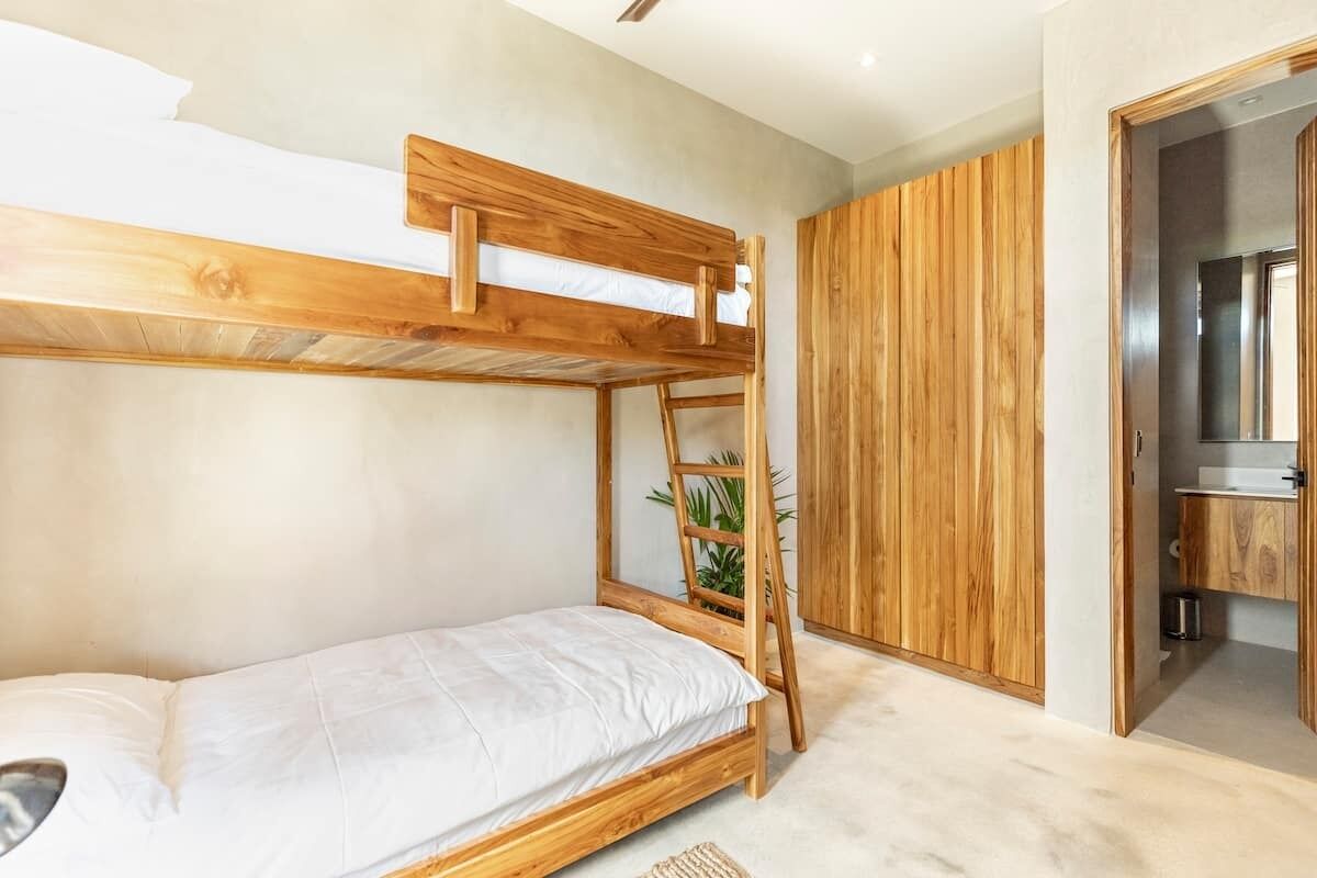 A bunk bed with a ladder, a small plant, and a wooden wardrobe in a room with a kitchenette.
