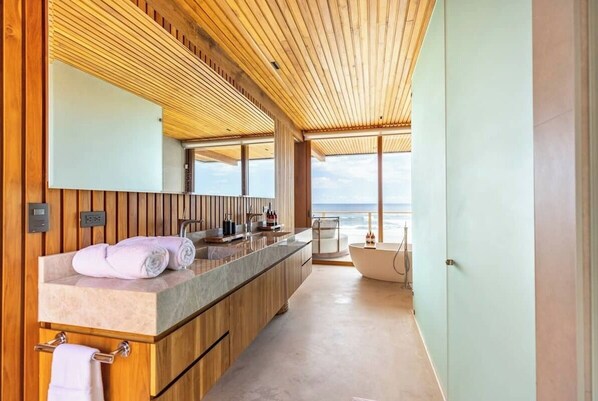 A modern bathroom with a wooden vanity, a large mirror, and a bathtub.
