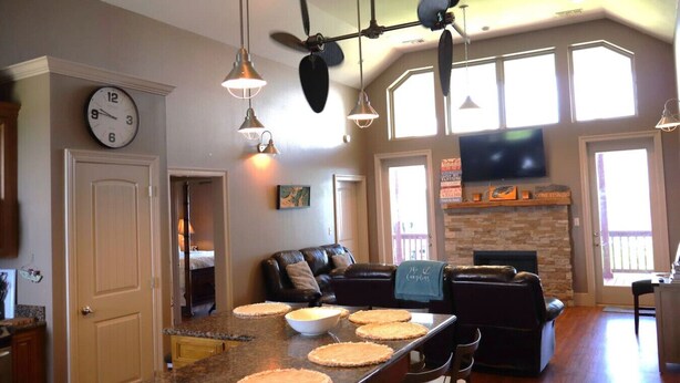 A spacious living area with a fireplace, a dining table with pies, and a large clock on the wall. - East Camptons-Lakehouse And Pool (New Orleans)