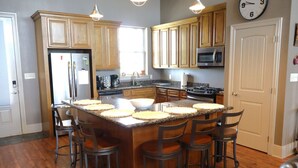 A kitchen with wooden cabinets, a central island with stools, a refrigerator, a microwave, and a stove. - East Camptons-Lakehouse And Pool (New Orleans)
