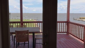 A covered outdoor area with a table and chairs, overlooking a body of water and a dock. - East Camptons-Lakehouse And Pool (New Orleans)