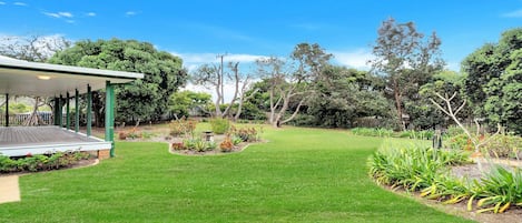 Un jardín bien cuidado con una terraza de madera, diversas plantas y un cielo azul despejado.