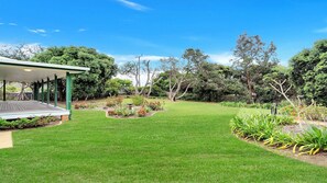 Un giardino curato con un’elegante terrazza in legno, diverse piante e un cielo azzurro.