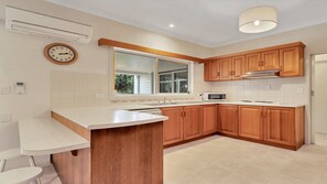 A modern kitchen with wooden cabinets, a white countertop, a built-in microwave, and a window with blinds. - Birdsong - Central location (Wooli)