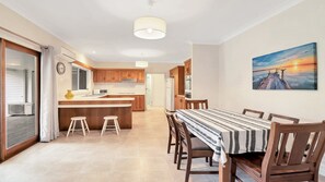 A modern kitchen with wooden cabinets, a central island, and a dining area with a striped tablecloth. - Birdsong - Central location (Wooli)