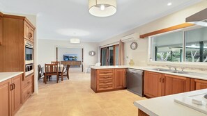 A modern kitchen with wooden cabinets, a built-in oven, a dishwasher, and a large window offering a view of the outdoors. - Birdsong - Central location (Wooli)