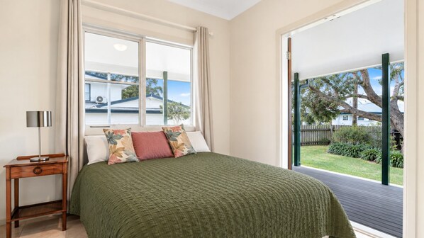 A bedroom with a bed, a nightstand, a window with curtains, and a view of the outdoors. - Birdsong - Central location (Wooli)