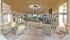 A spacious indoor area with striped chairs and tables, a ceiling fan, and signs for a restaurant and grocery store. - 4BR Disney | Windsor Hills Resort | Pool Villa (Kissimmee)