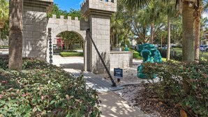 A stone archway leading to a castle-like structure, surrounded by palm trees and greenery. - 4BR Disney | Windsor Hills Resort | Pool Villa (Kissimmee)