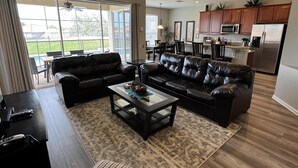 A spacious living room with two black leather sofas, a coffee table, and a dining area with chairs. - 4BR Disney | Windsor Hills Resort | Pool Villa (Kissimmee)