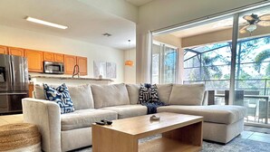 A modern living room with a sectional sofa, a wooden coffee table, and a kitchen in the background. - Disney | Pool&Spa | Windsor Hills | Privacy | Amazing Views (Kissimmee)