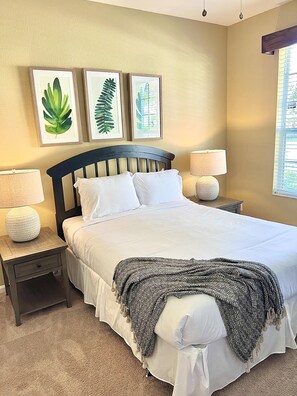 Cozy retreat with a large bed, dark headboard, and bedside lamps, accompanied by framed botanical prints.