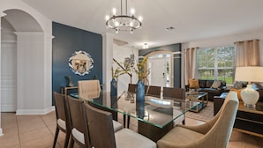 Un soggiorno moderno con un tavolo da pranzo in vetro, divani scuri e un lampadario.