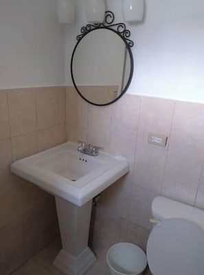 A bathroom with a pedestal sink, a round mirror, and a toilet.