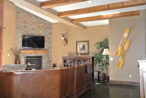 Un salon avec une cheminée en briques, une tête de cerf accrochée au mur, un téléviseur, un canapé et des paires de skis fixés au mur.