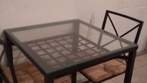 Ein Tisch mit Glasplatte, Holzstühle, einem Metallgestell und einem Fliesenboden.