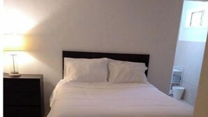 Ein ordentlich bezogenes Bett in einem Zimmer mit Fliesenboden und einem Nachttisch mit Lampe.